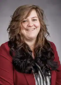Ginger Research and Production Facility Woman with long wavy hair smiling, wearing a red blazer.